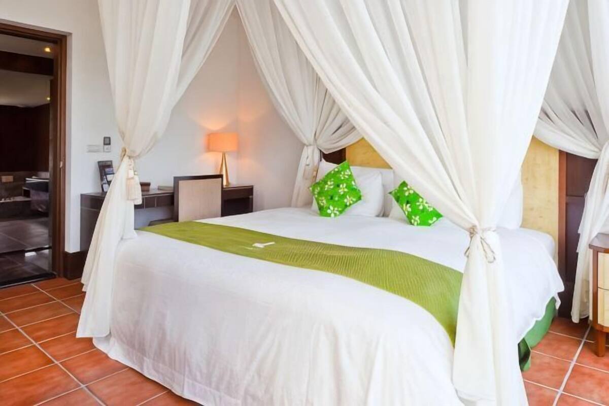 A bed with a canopy, a bedside table, a lamp, and a green throw blanket.