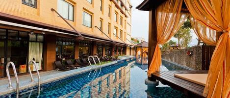 Un espace piscine d’hôtel avec une piscine carrelée, des chaises longues et un bâtiment doté de grandes fenêtres.