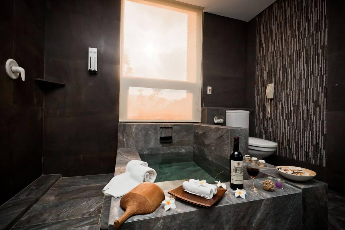 A modern bathroom with a large bathtub, a toilet, and a shower area. There is a bottle of wine and a bowl of fruit on the counter.