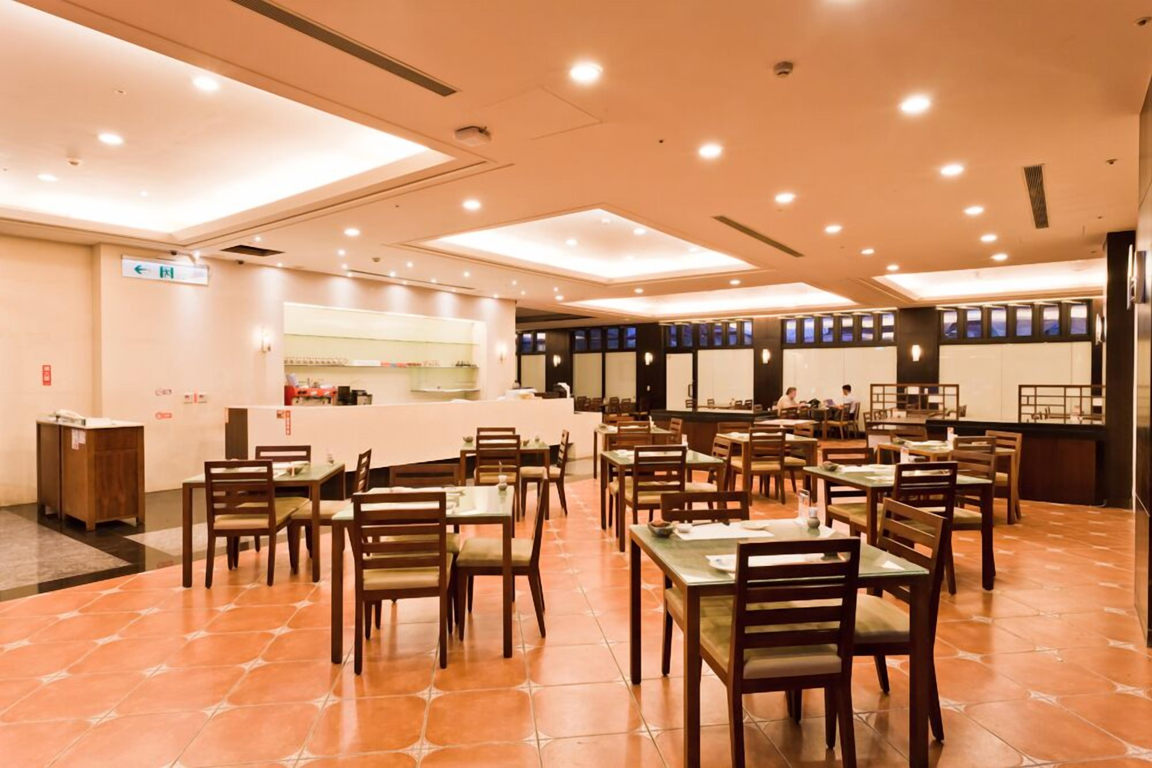 A spacious restaurant with multiple tables and chairs, a counter for ordering, and a tiled floor.