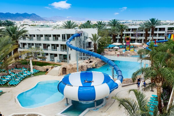 Parque aquático com um escorregador grande, piscina e área de descanso com cadeiras.