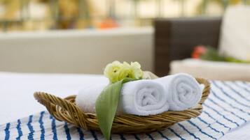 A wicker basket with rolled white towels and a yellow flower on a striped cloth.