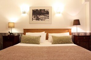 A neatly made bed with a patterned blanket, two pillows, and a framed cityscape picture on the wall. - Hudsons (Brighton)
