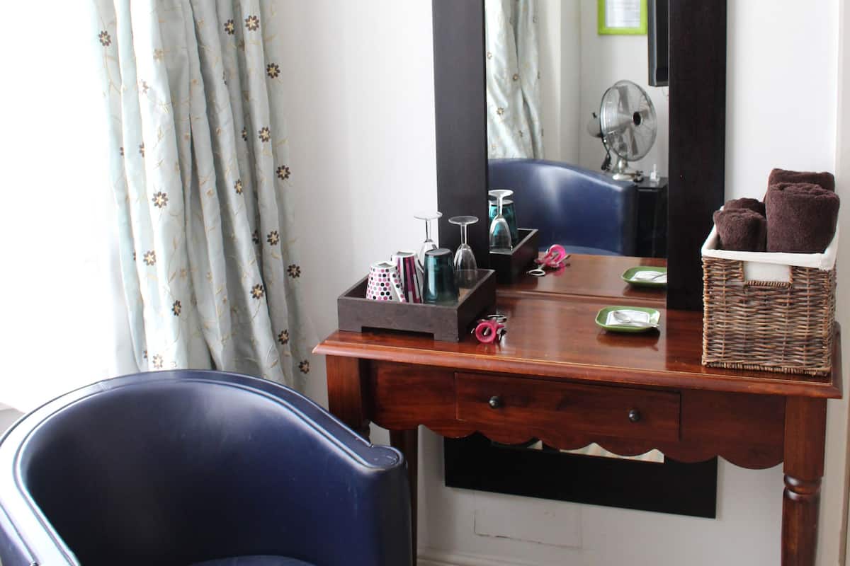 Quarto com escrivaninha de madeira, uma cadeira azul, um espelho grande e uma cesta de vime com toalhas.