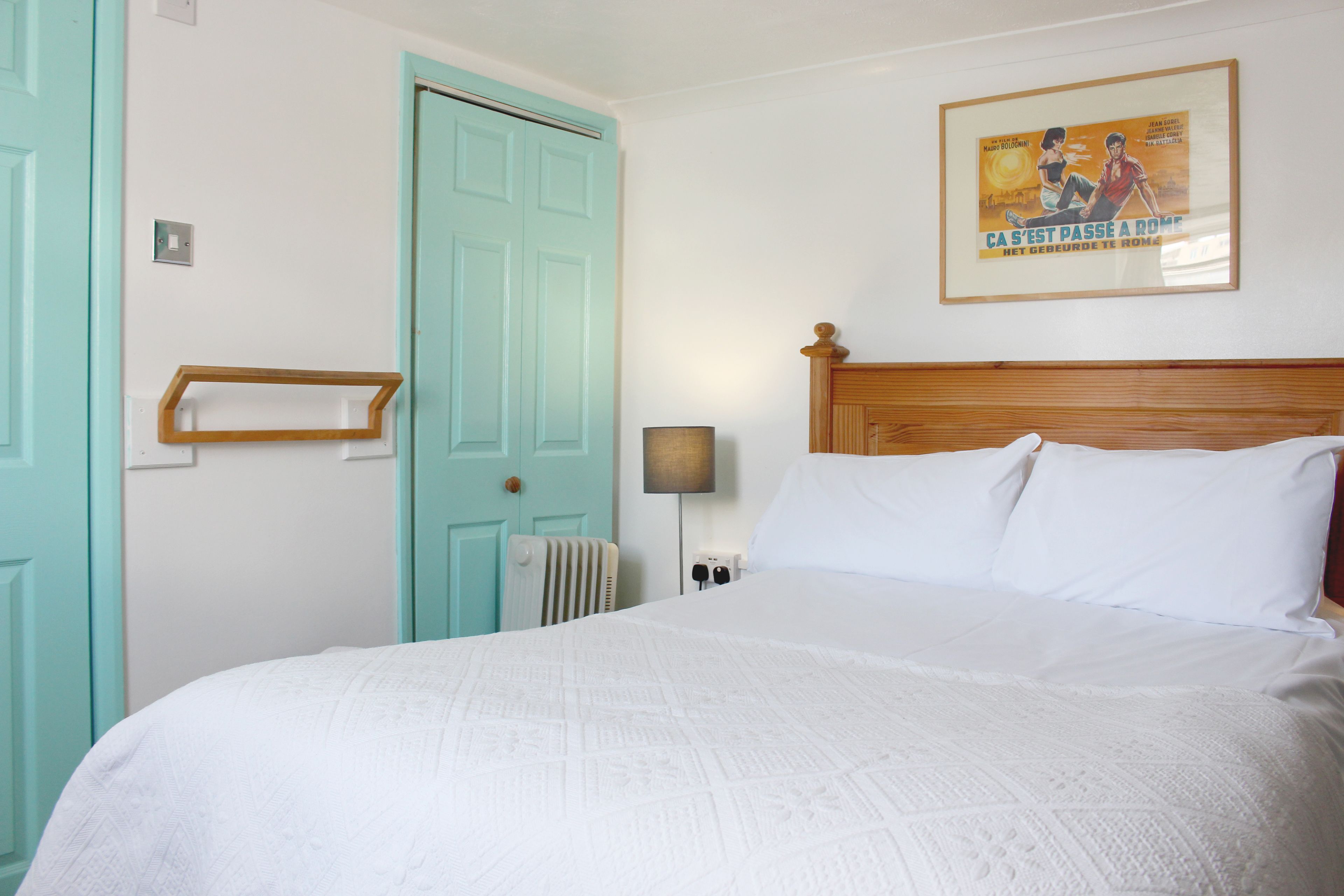A bedroom with a bed, a wooden headboard, a wall-mounted lamp, a radiator, and a door.