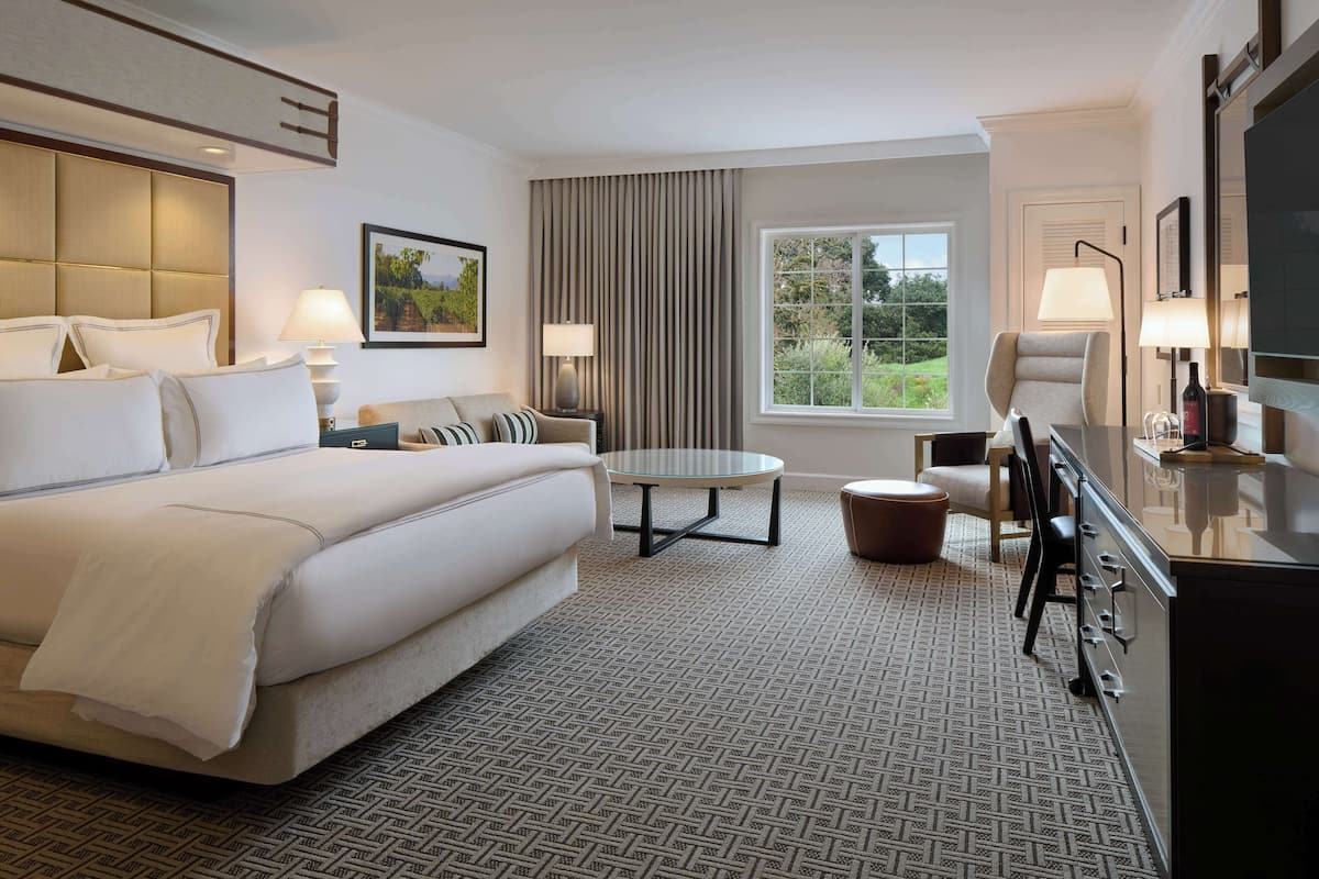 A hotel room with a large bed, a round table, a sofa, a chair, and a desk with a lamp.