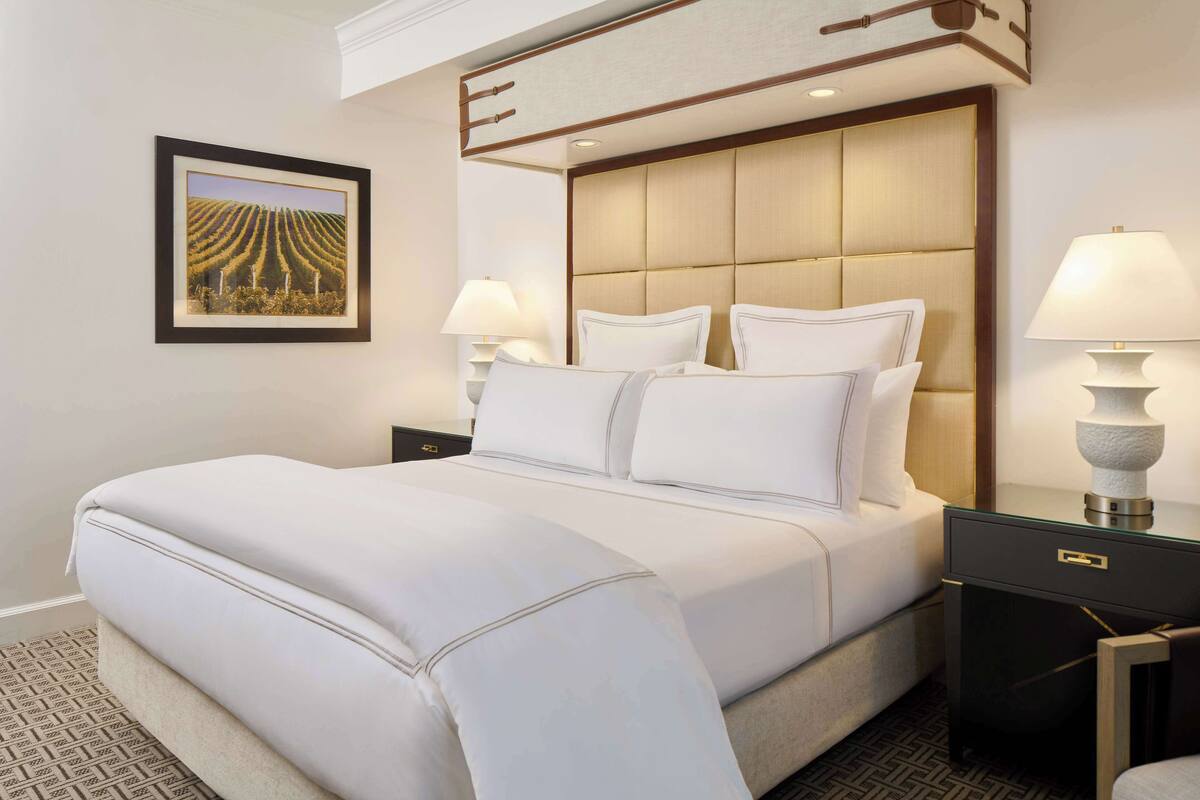 A hotel room with a large bed, two bedside tables, and a framed picture on the wall.