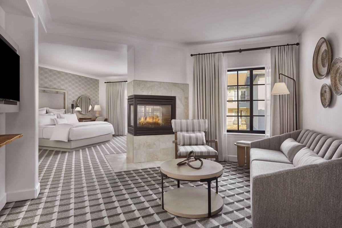 A modern hotel room with a fireplace, a sofa, a chair, and a bed.