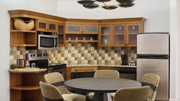 A kitchen with wooden cabinets, a microwave, a refrigerator, and a round dining table with chairs.
