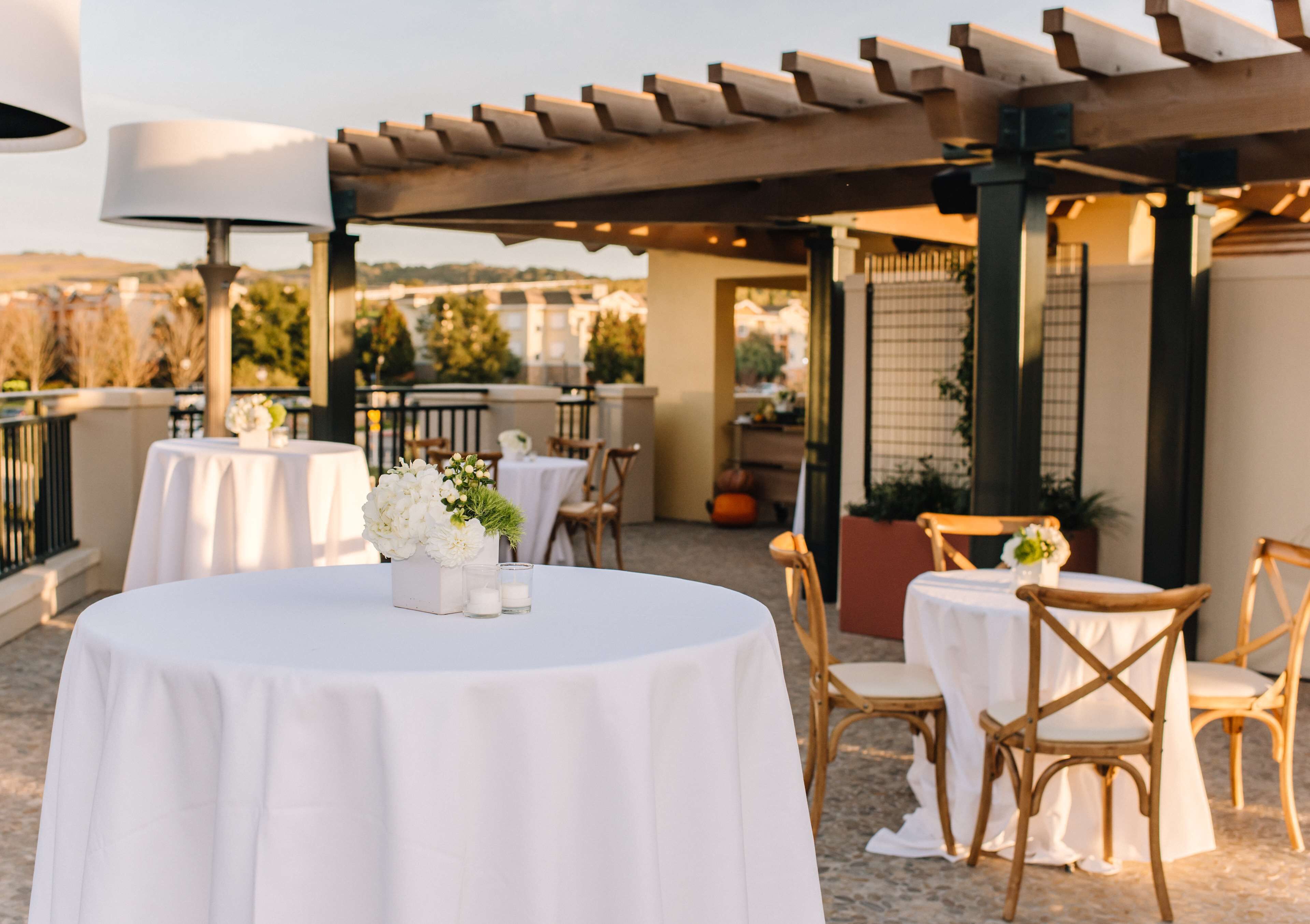Una terrazza sul tetto con tavoli e sedie rotonde, coperta da una pergola, e circondata da un muretto.