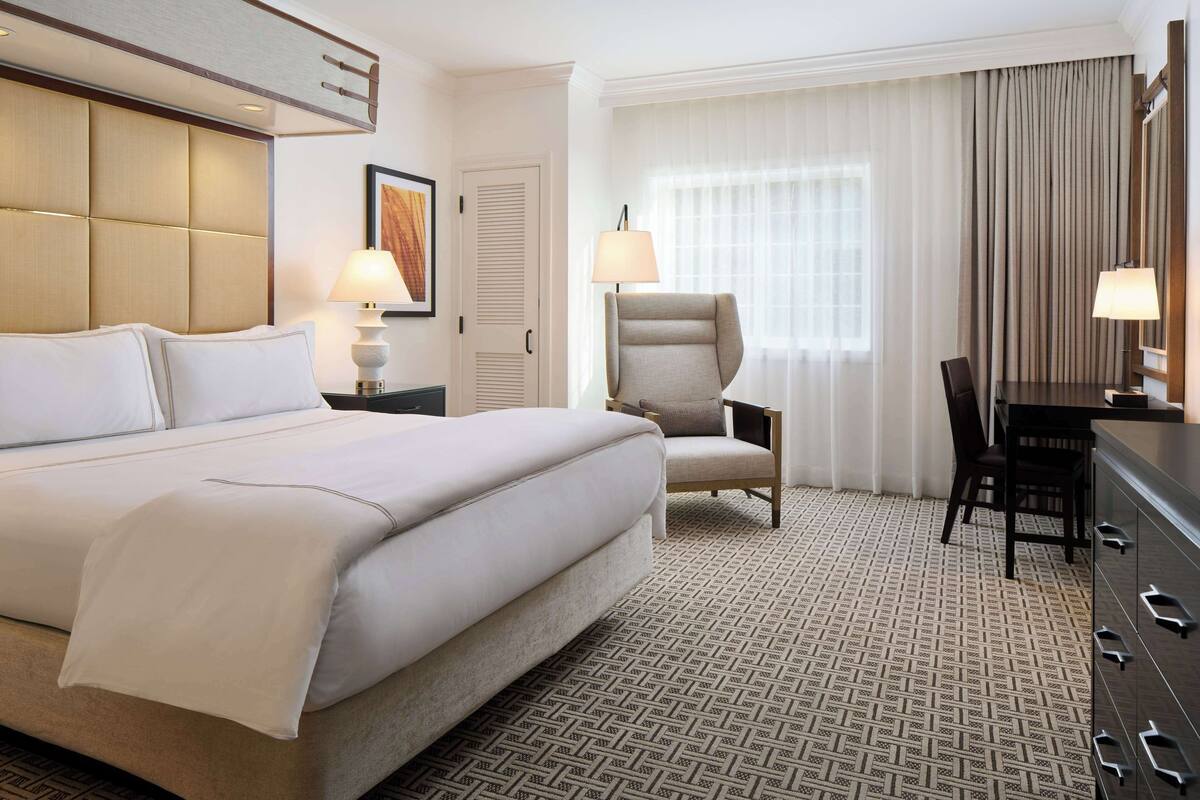 A hotel room with a large bed, a desk, a chair, and a lamp.