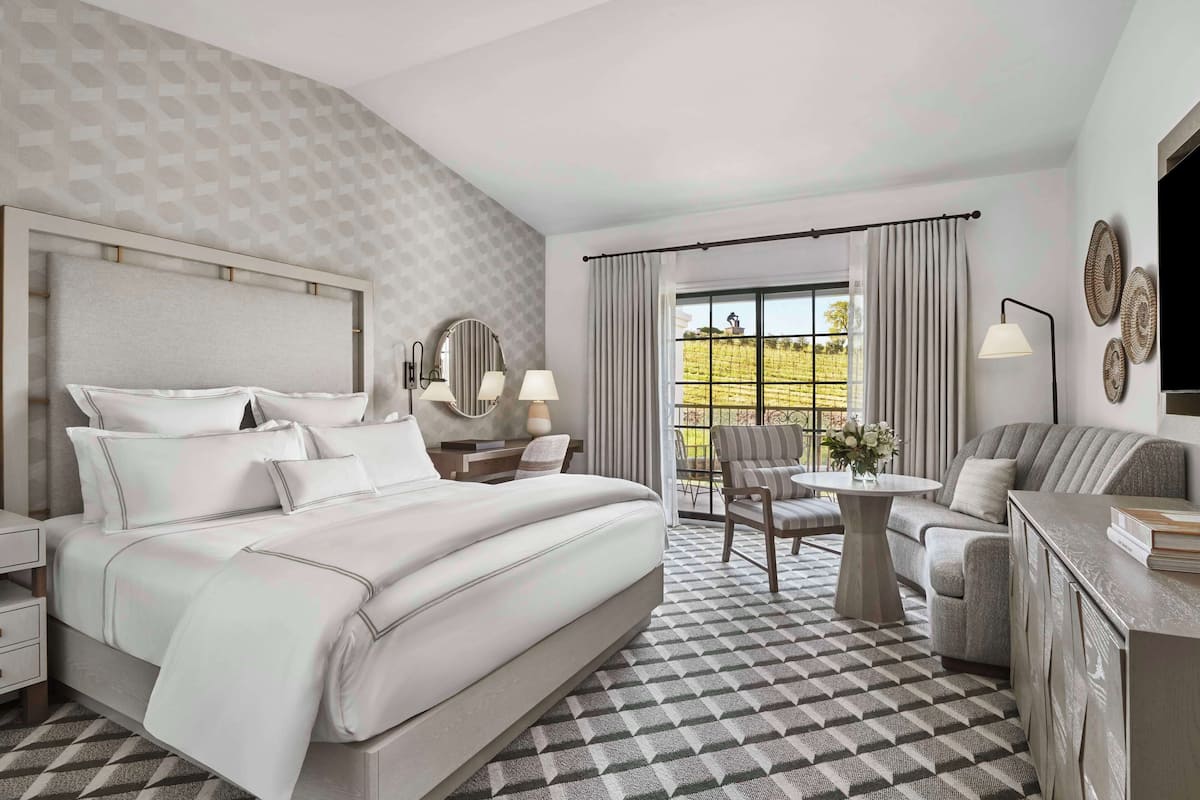 A hotel room with a large bed, a sofa, a dining table, and a balcony with curtains.