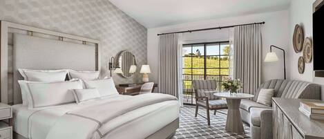 A hotel room with a large bed, a sofa, a dining table, and a balcony with curtains.