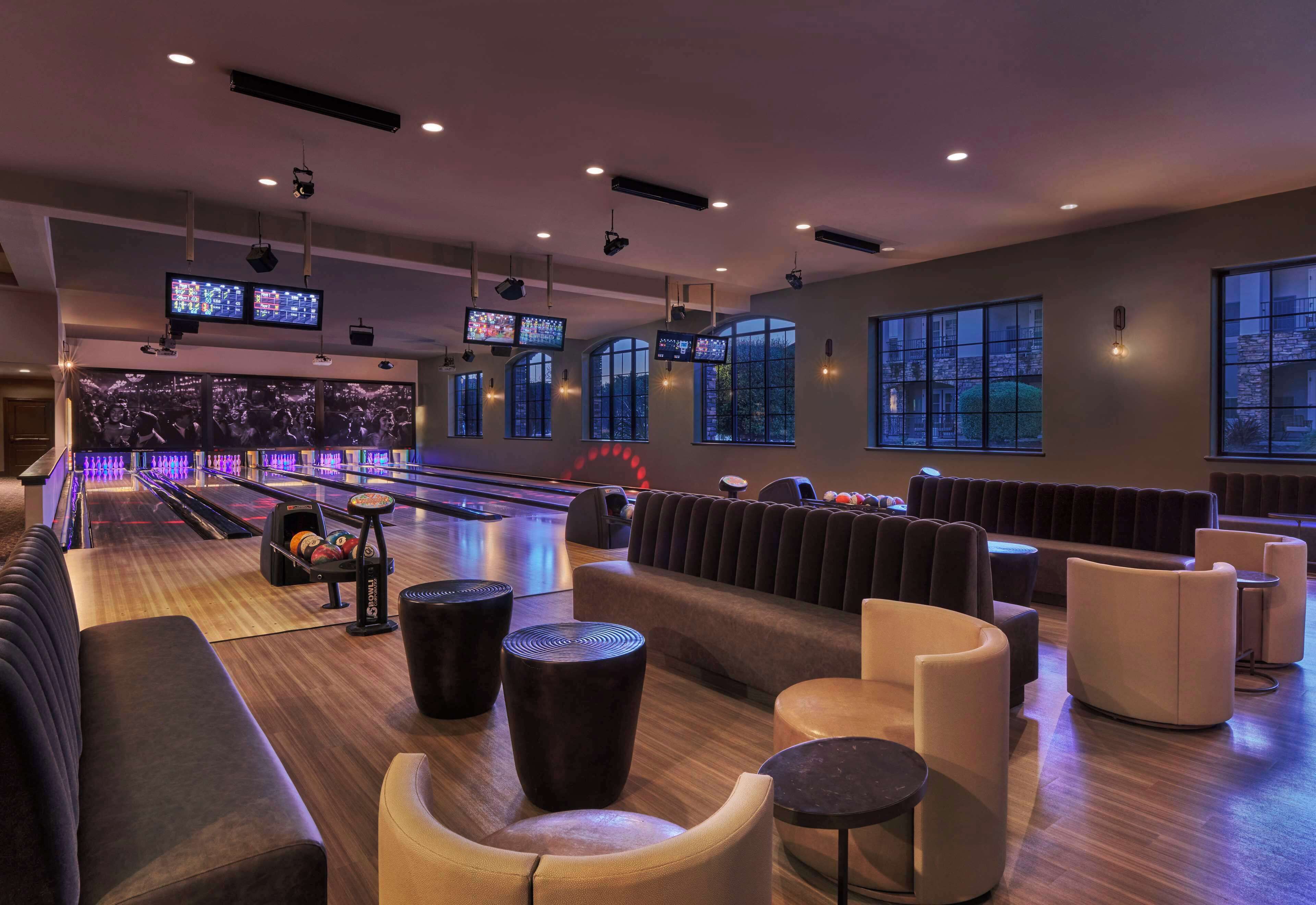 A bowling alley with seating areas and multiple screens displaying games.