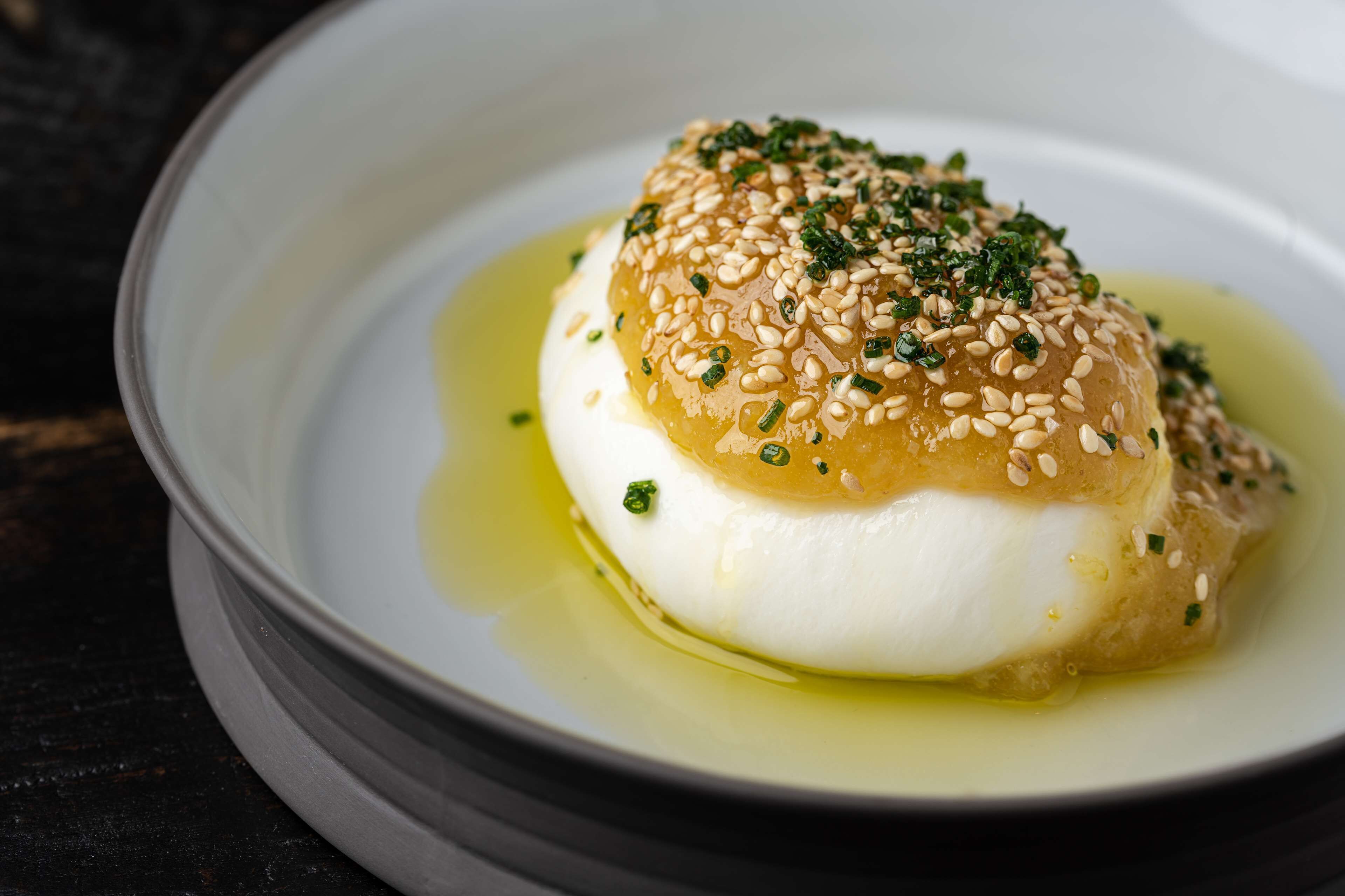 A dish with a white base topped with sesame seeds and green herbs, served in a white bowl with a liquid base.