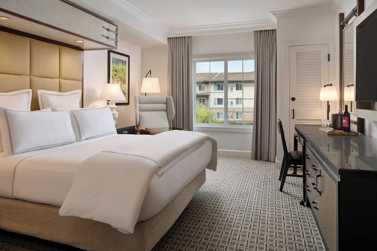 A hotel room with a large bed, a desk with a chair, a TV, and a window with a view of buildings.