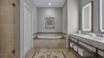 A modern bathroom with a bathtub, two sinks, a large mirror, and a patterned rug.