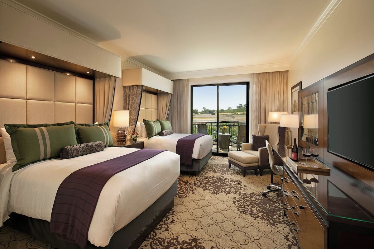 A hotel room with two beds, a sofa, a TV, and a balcony with a view.