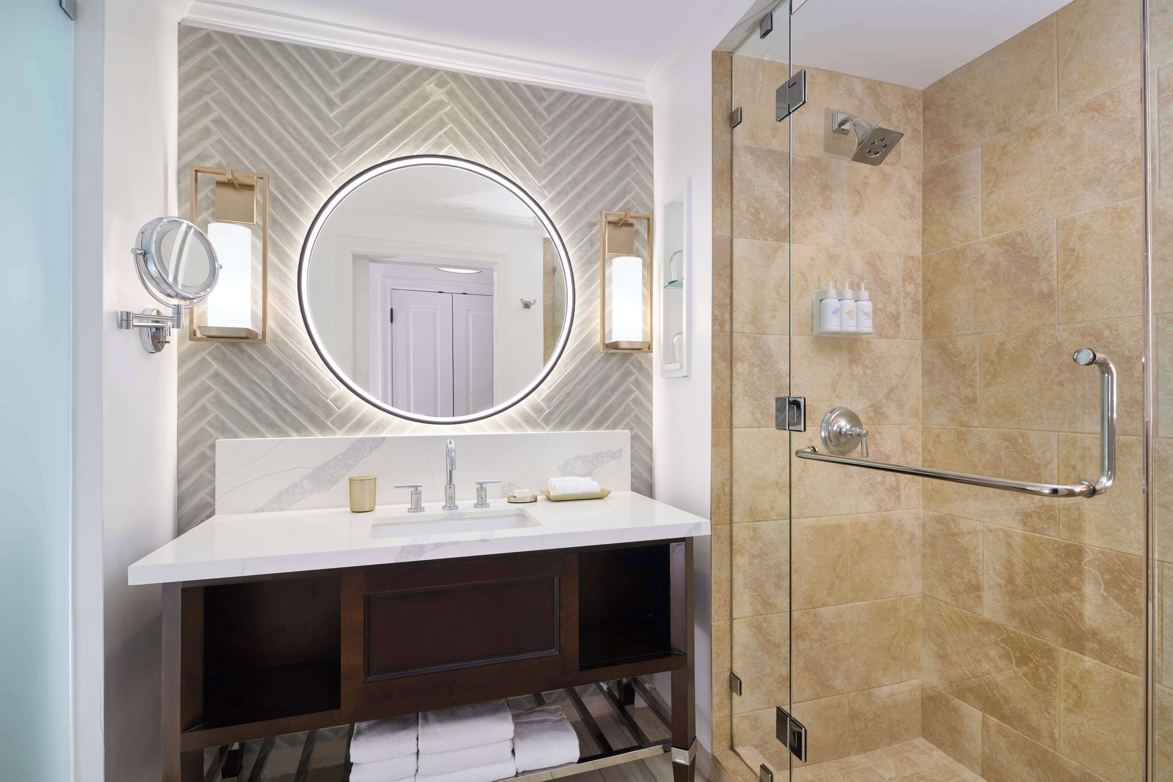 A modern bathroom with a large mirror, a vanity with a sink, and a glass-enclosed shower area.