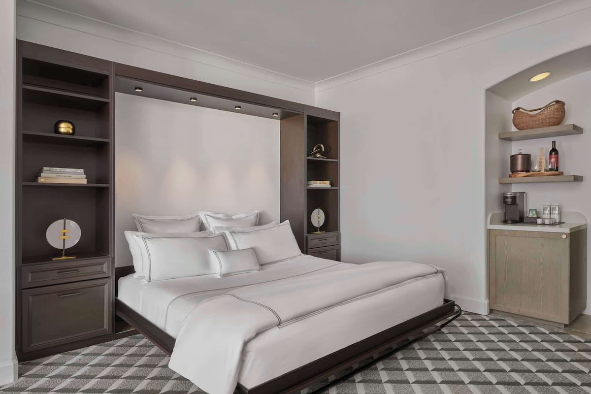 A modern bedroom with a large bed, built-in shelving, and a small kitchenette.
