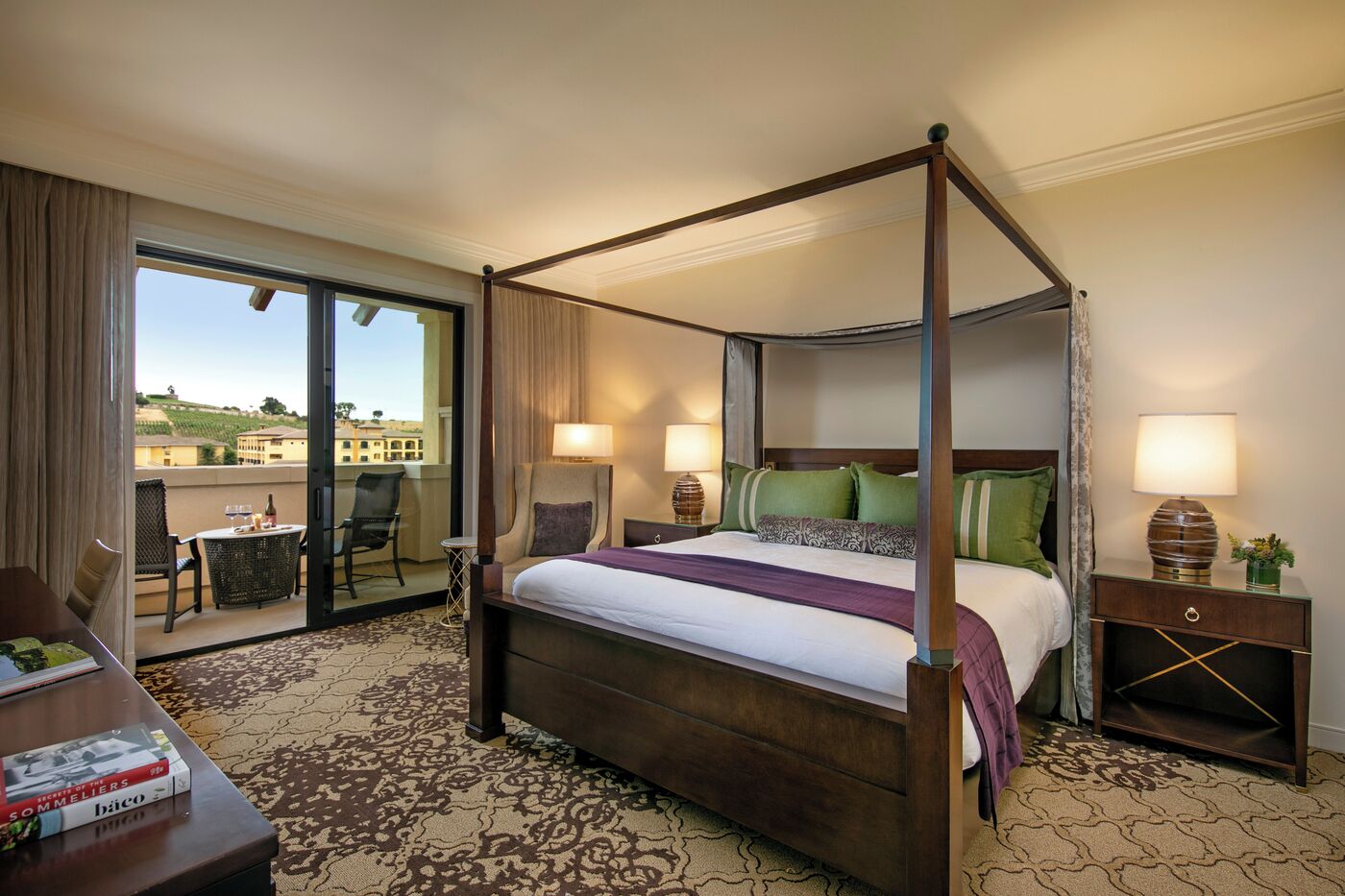 A four-poster bed with a view of a vineyard through the balcony doors.