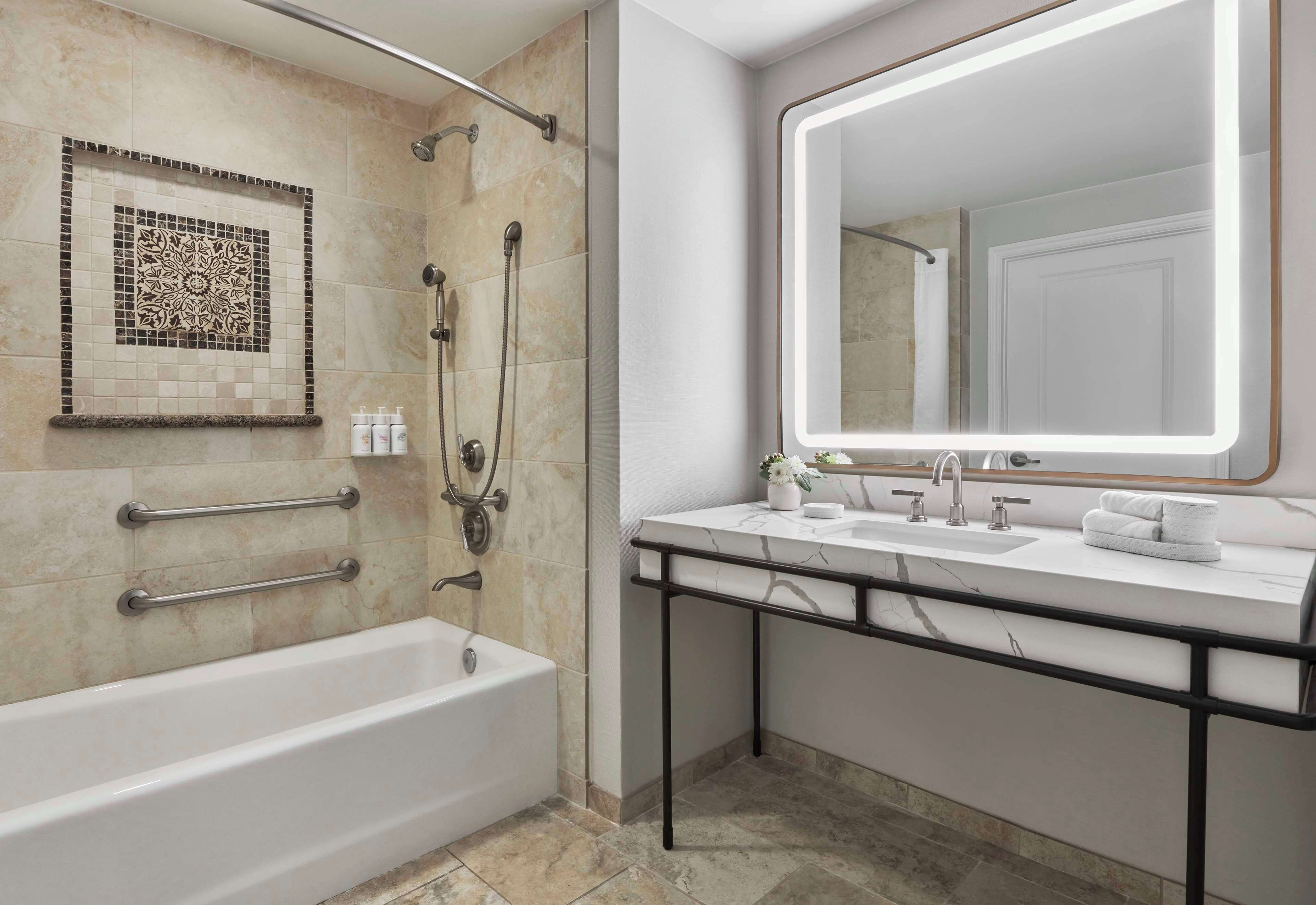 Une salle de bain moderne avec une baignoire, une douche avec une porte en verre, un meuble-lavabo doté d’un grand miroir et un mur décoratif recouvert de carreaux.