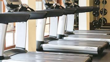 En række Life Fitness løbebånd i et fitnesscenter med store vinduer og et vægtstativ i baggrunden.