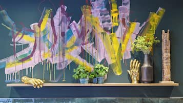 Una pared con arte abstracto, una repisa con plantas y un jarrón.