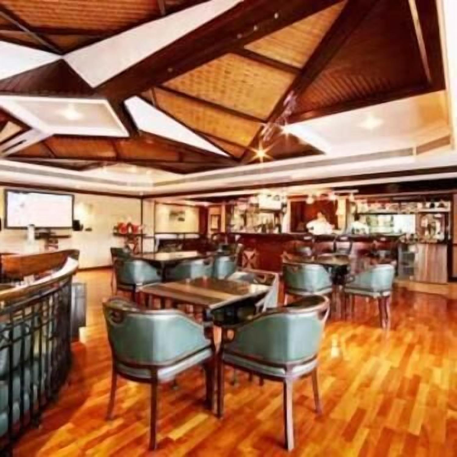 A restaurant with wooden flooring, green upholstered chairs, and a bar area.