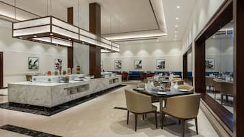 A modern hotel lobby with a marble reception desk, dining area with tables and chairs, and artwork on the walls.