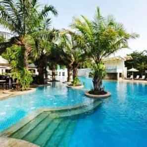 Una piscina con agua cristalina y azul, rodeada de palmeras y sillas de descanso.