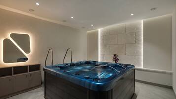 A modern bathroom with a large bathtub, recessed ceiling lights, and a decorative wall panel.