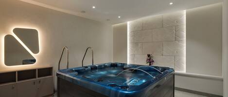 A modern bathroom with a large bathtub, recessed ceiling lights, and a decorative wall panel.