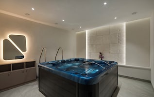 A modern bathroom with a large bathtub, recessed ceiling lights, and a decorative wall panel.