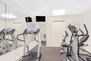 Un gimnasio con cintas de correr, equipamiento de ejercicio, un espejo y un cartel que indica el uso del centro.