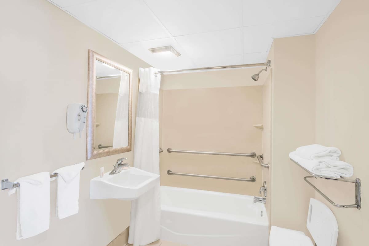 A bathroom with a sink, mirror, towel rack, and a shower area with a grab bar.