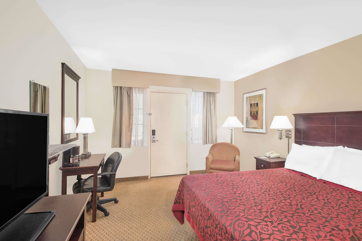 A hotel room with a bed, desk, chair, TV, and lamps.
