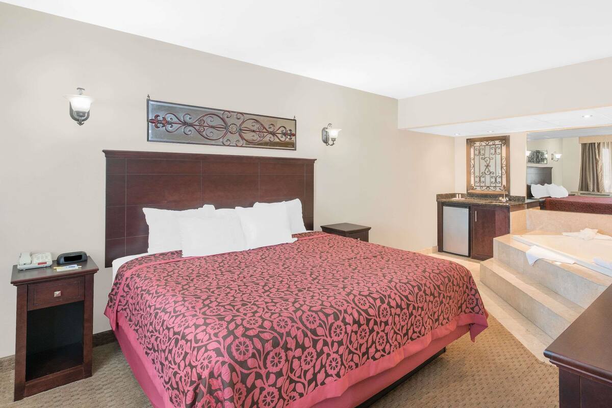 A hotel room with a large bed, a nightstand, a desk, a mirror, and a bathroom visible through an open door.