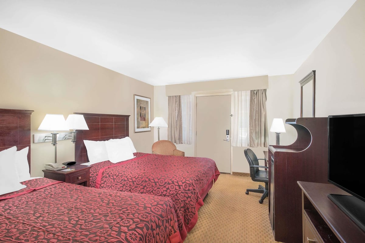 A hotel room with two beds, a desk, a chair, a TV, and a door.