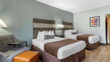 A hotel room with two beds, a sofa, a small table, and a wall-mounted lamp.
