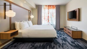 A hotel room with a large bed, bedside tables, a TV, and a window with curtains.