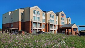 A multi-story hotel with a central entrance, balconies, and a landscaped garden area.