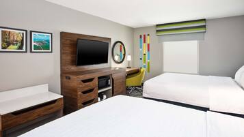 A hotel room with two beds, a desk, a flat-screen TV, a mirror, and a window with blinds.