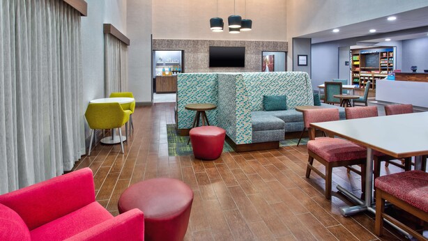 A modern hotel lobby with a seating area, a reception desk, and a dining area. - Hampton Inn & Suites - Cape Coral/Fort Myers Area, FL (Cape Coral)