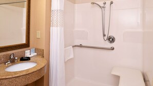 A bathroom with a granite sink, a mirror, a shower with a handheld showerhead, and a grab bar.