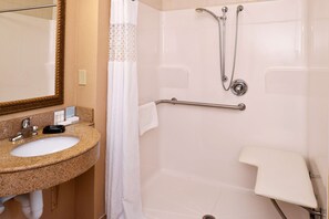 A bathroom with a granite sink, a mirror, a shower with a handheld showerhead, and a grab bar.