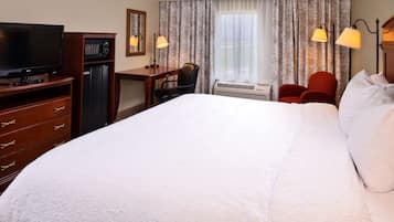 A hotel room with a bed, a desk, a chair, a television, and a heater.