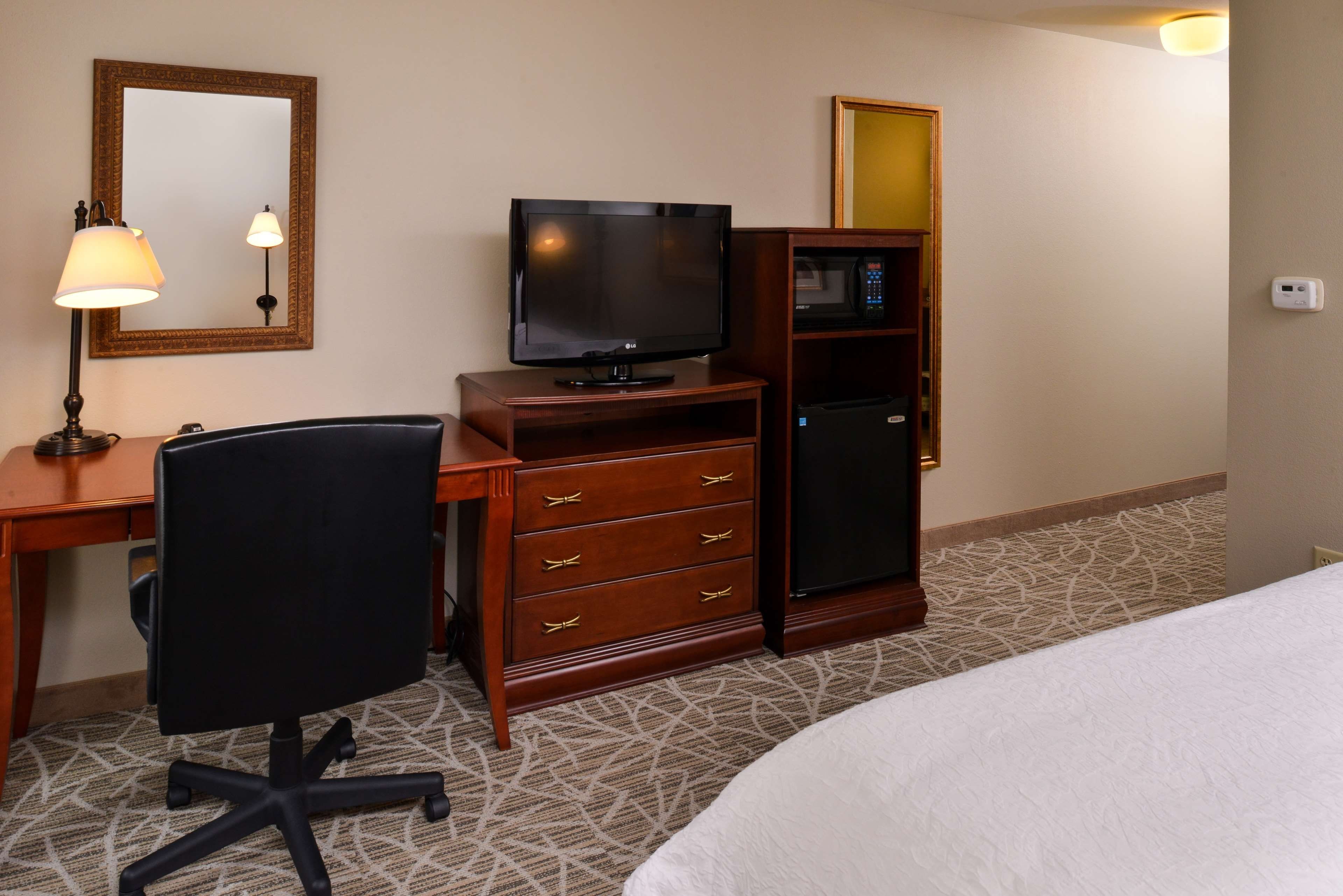 Ein Hotelzimmer mit Bett, Schreibtisch mit Stuhl, Fernseher, Minibar und Spiegel.