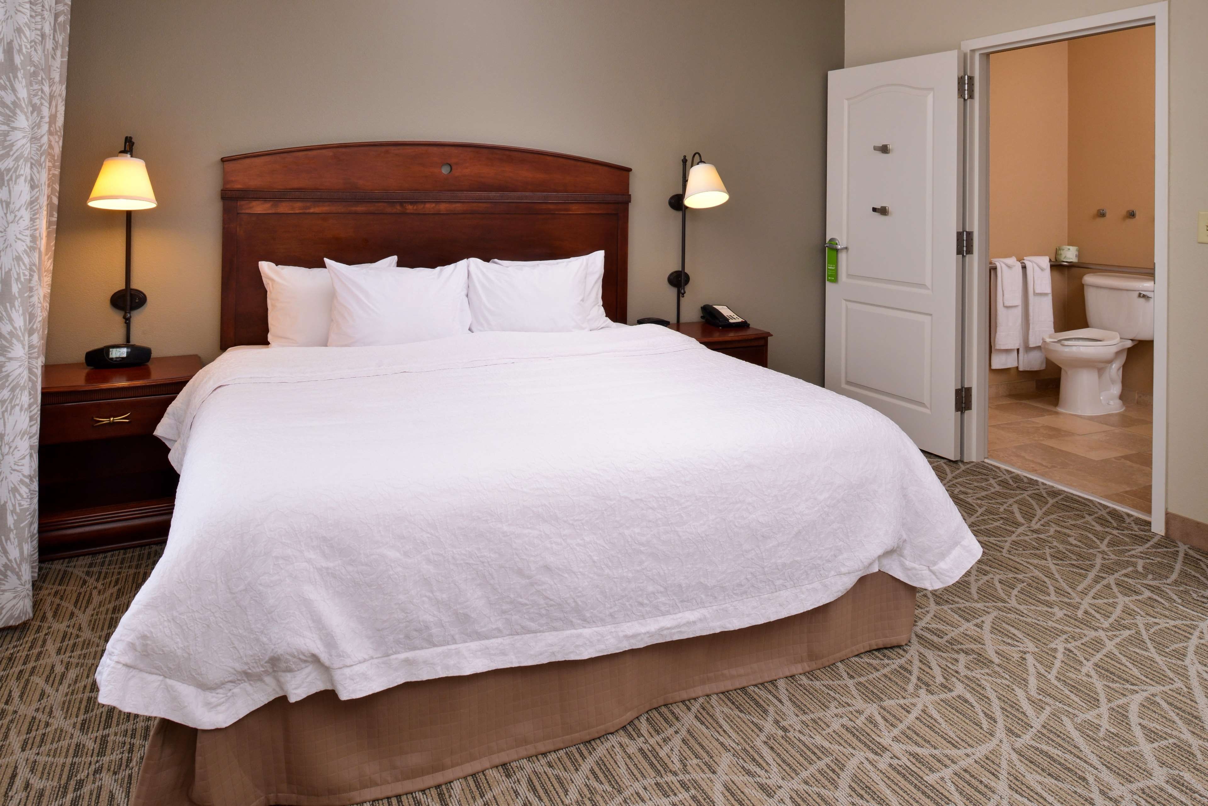 A hotel room with a large bed, bedside lamps, a nightstand, and a bathroom visible through an open door.