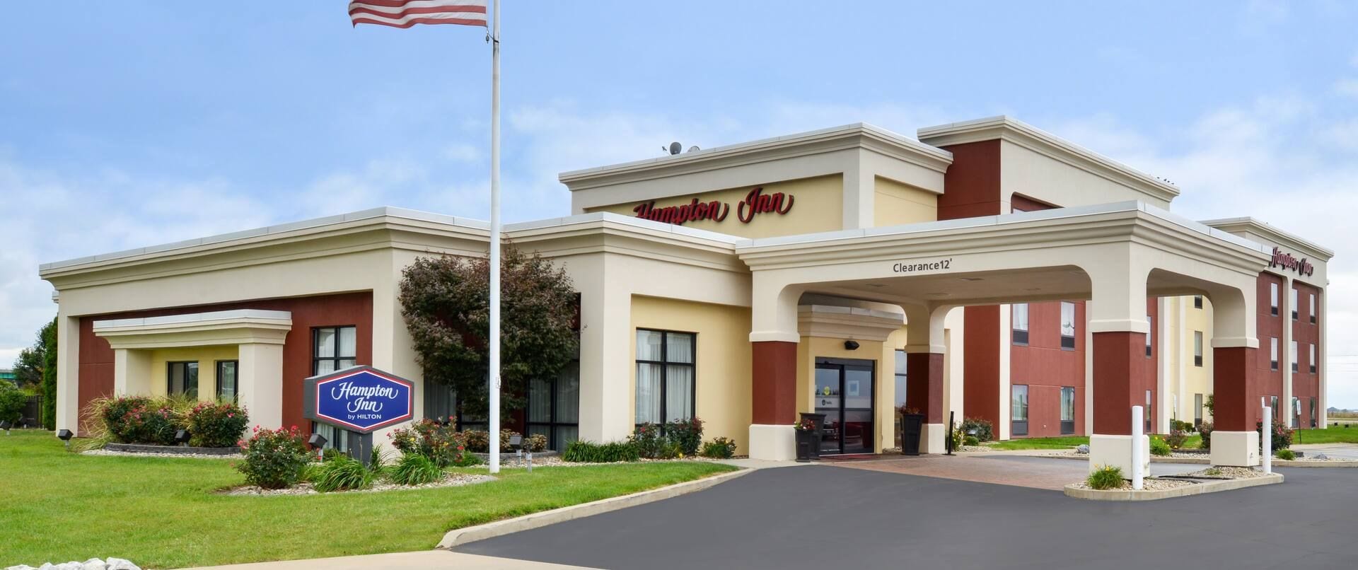 A Hampton Inn by Hilton hotel with a clear entrance, a flag, and a sign indicating a 12-foot clearance.